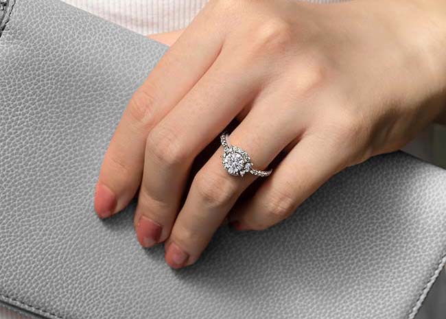 Woman wearing a moissanite ring holding a grey purse